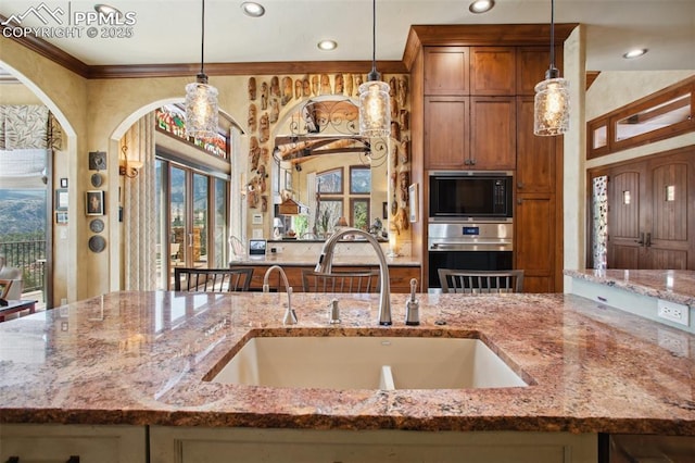 kitchen featuring light stone counters, decorative light fixtures, a sink, black microwave, and oven