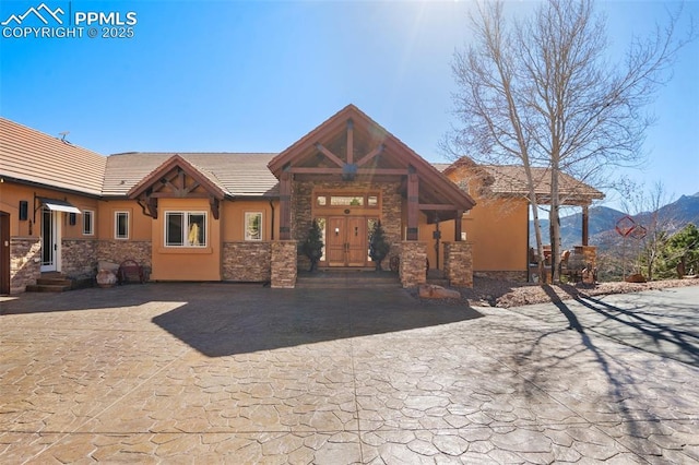 view of front facade featuring stone siding, a tile roof, a mountain view, and stucco siding