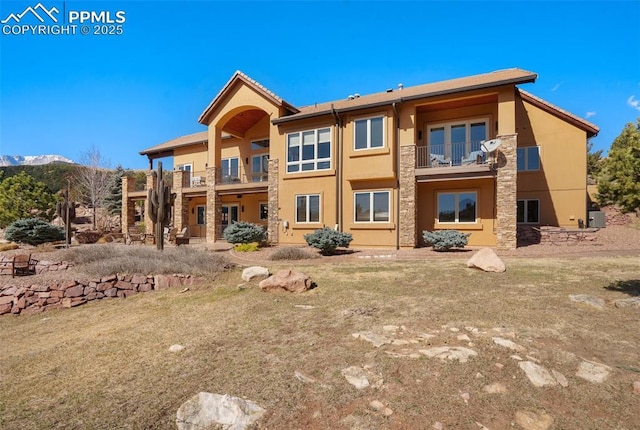 back of house featuring a mountain view, stone siding, a balcony, and stucco siding