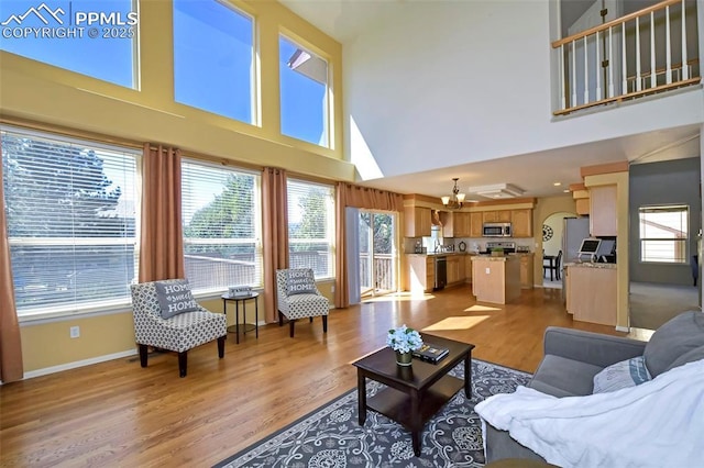 living area with baseboards, light wood-type flooring, and a towering ceiling