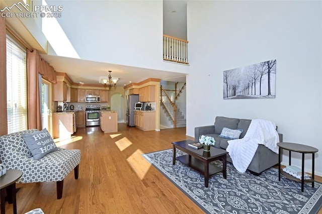 living room featuring light wood-type flooring, a chandelier, baseboards, a towering ceiling, and stairs