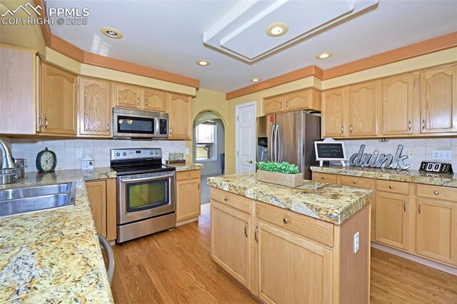 kitchen with a kitchen island, light brown cabinetry, appliances with stainless steel finishes, light wood-style floors, and a sink