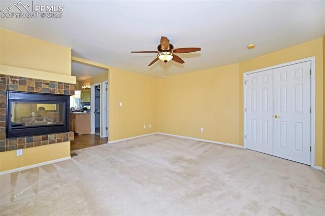 unfurnished living room with a tiled fireplace, baseboards, carpet, and a ceiling fan