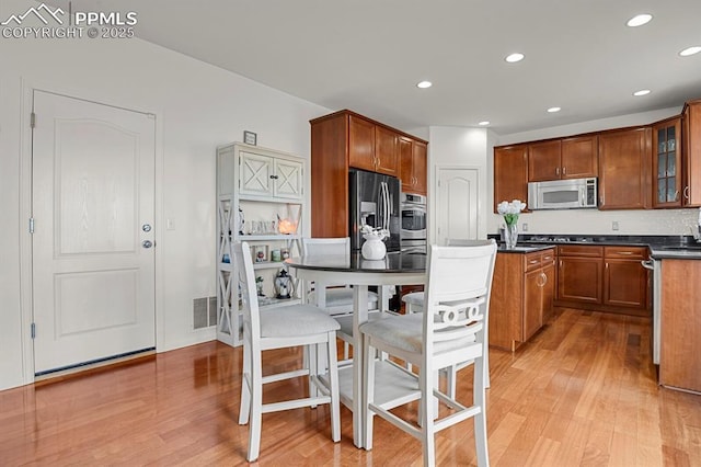 kitchen featuring light wood finished floors, dark countertops, appliances with stainless steel finishes, and brown cabinetry