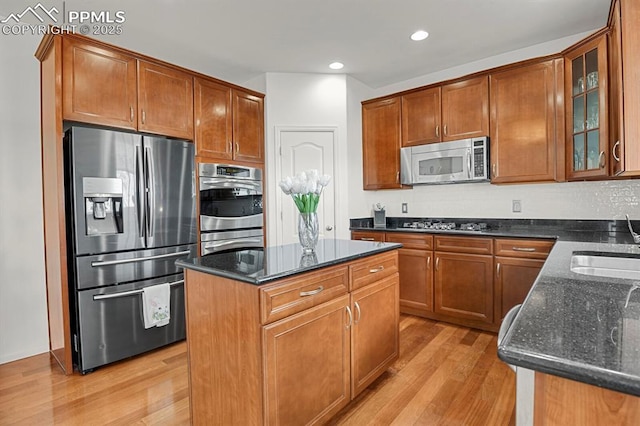 kitchen with dark stone countertops, a kitchen island, light wood-style flooring, stainless steel appliances, and glass insert cabinets