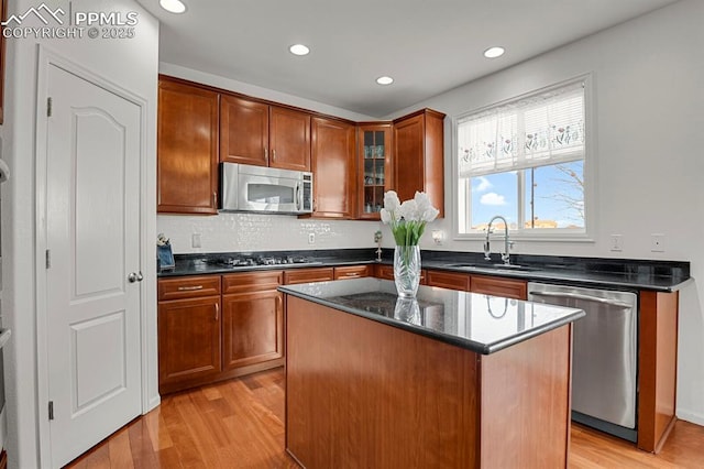 kitchen with light wood finished floors, appliances with stainless steel finishes, glass insert cabinets, and a sink