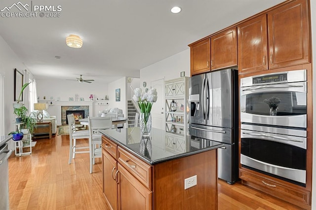 kitchen featuring light wood finished floors, a center island, a stone fireplace, appliances with stainless steel finishes, and a ceiling fan