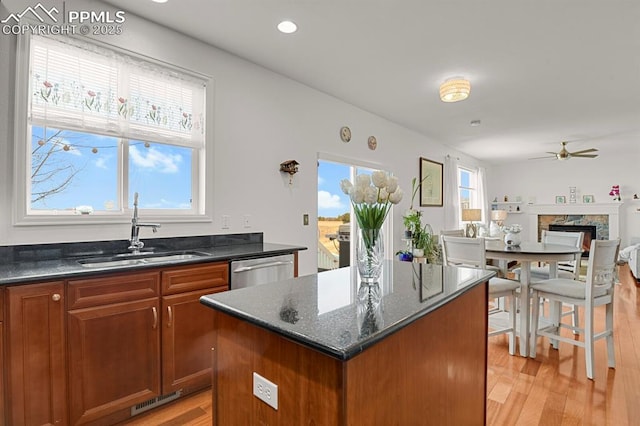 kitchen with a sink, dark stone countertops, stainless steel dishwasher, a center island, and light wood-style floors