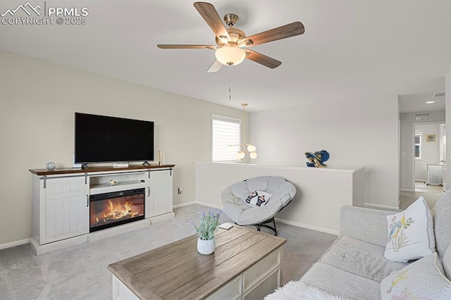 living area with a glass covered fireplace, light colored carpet, baseboards, and ceiling fan