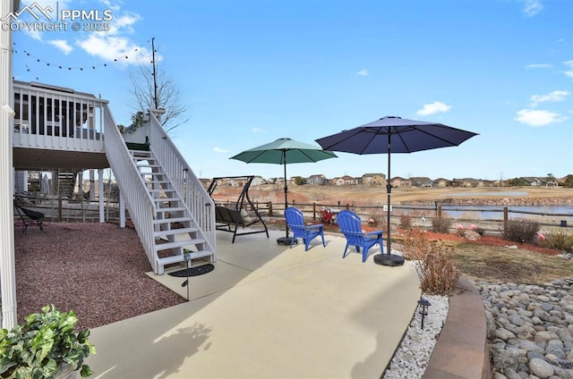 view of playground with stairway, a deck with water view, a patio, and fence