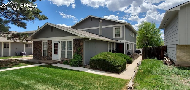 traditional home with stone siding, a front lawn, fence, and stucco siding