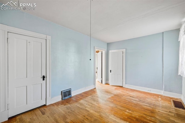 unfurnished room with baseboards, visible vents, and hardwood / wood-style floors