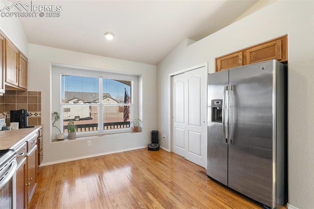 kitchen featuring tasteful backsplash, lofted ceiling, stainless steel appliances, light countertops, and light wood-style floors