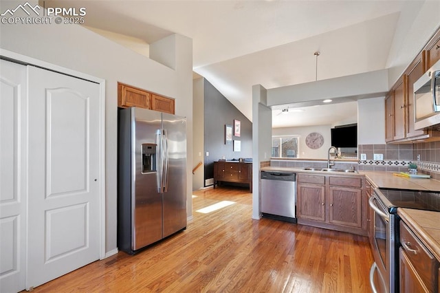 kitchen featuring light wood-style flooring, a sink, appliances with stainless steel finishes, backsplash, and brown cabinets