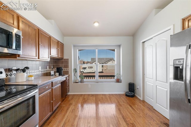 kitchen featuring lofted ceiling, light wood-style flooring, appliances with stainless steel finishes, brown cabinets, and tasteful backsplash