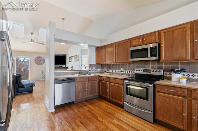 kitchen with stainless steel appliances, backsplash, a sink, and brown cabinets