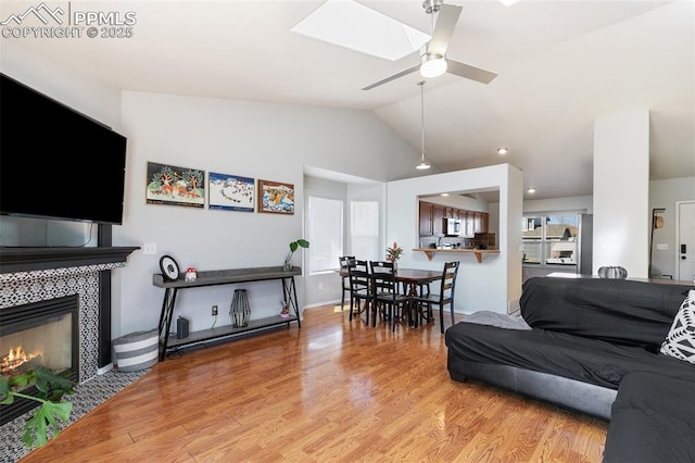 living room featuring lofted ceiling with skylight, a fireplace, wood finished floors, and a ceiling fan