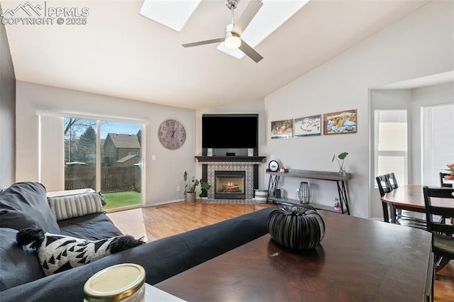 living area with a ceiling fan, vaulted ceiling with skylight, a tiled fireplace, and wood finished floors