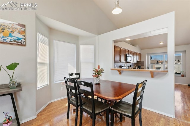 dining area with vaulted ceiling, light wood-style flooring, and baseboards