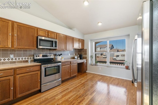 kitchen with lofted ceiling, stainless steel appliances, light wood-type flooring, tile counters, and brown cabinetry