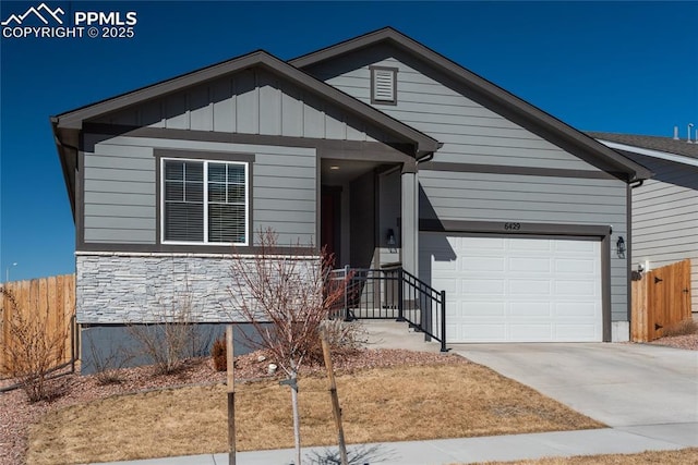 view of front of home with an attached garage, board and batten siding, fence, stone siding, and driveway