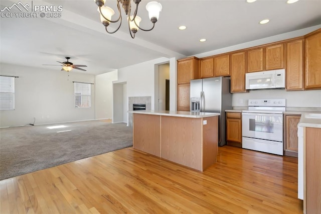 kitchen with light countertops, a tiled fireplace, open floor plan, a kitchen island, and white appliances