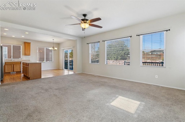 unfurnished living room with recessed lighting, ceiling fan with notable chandelier, light colored carpet, a sink, and baseboards