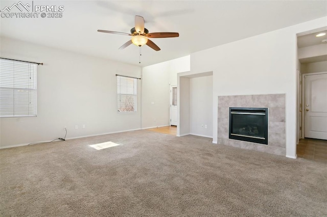 unfurnished living room with ceiling fan, a tiled fireplace, baseboards, and carpet flooring