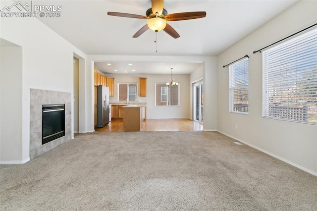 unfurnished living room featuring recessed lighting, light colored carpet, a tiled fireplace, baseboards, and ceiling fan with notable chandelier