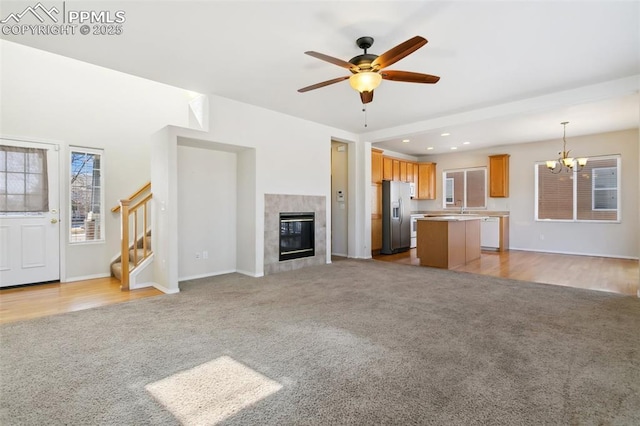 unfurnished living room with light colored carpet, ceiling fan with notable chandelier, recessed lighting, a premium fireplace, and stairway