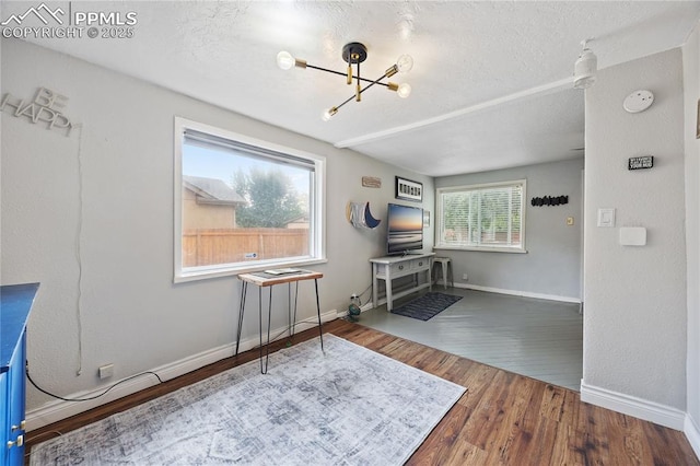 interior space with an inviting chandelier, a textured ceiling, baseboards, and wood finished floors