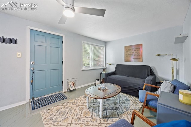 living area featuring a textured ceiling, baseboards, a ceiling fan, and wood finished floors