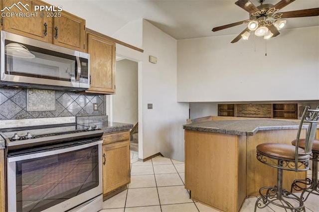 kitchen featuring light tile patterned flooring, appliances with stainless steel finishes, tile counters, tasteful backsplash, and a kitchen bar