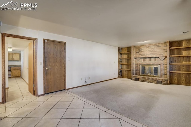 unfurnished living room featuring a brick fireplace, built in shelves, light tile patterned flooring, and light colored carpet