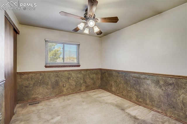 spare room with a wainscoted wall, carpet, visible vents, and a ceiling fan