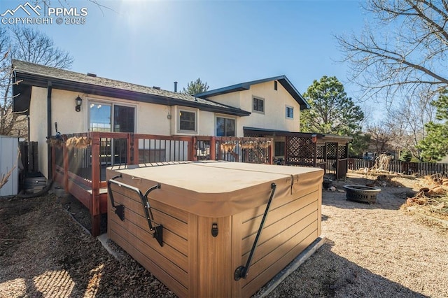 back of house with fence, a hot tub, a wooden deck, and stucco siding