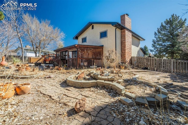 back of property with a chimney, fence, a deck, and stucco siding