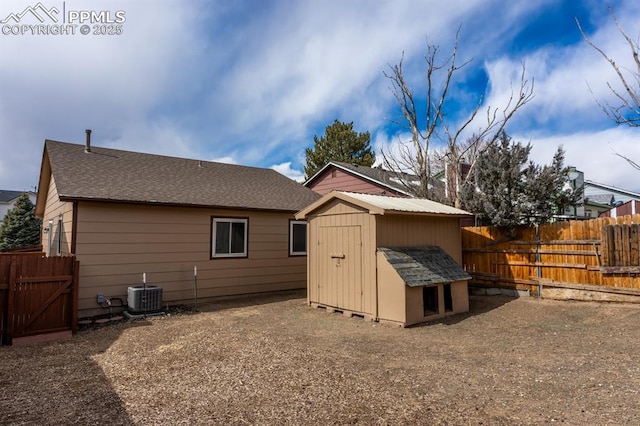 back of property with a shingled roof, a fenced backyard, cooling unit, an outdoor structure, and a shed