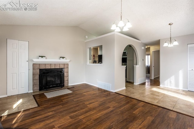 unfurnished living room with a chandelier, visible vents, a fireplace, and wood finished floors