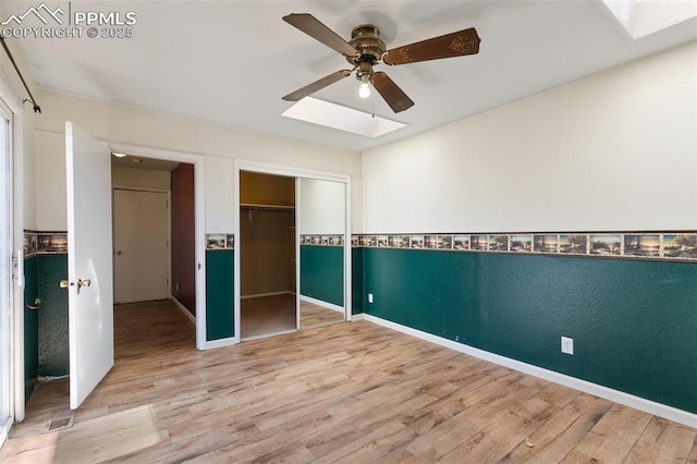 unfurnished bedroom with a ceiling fan, a skylight, a closet, and light wood-style flooring