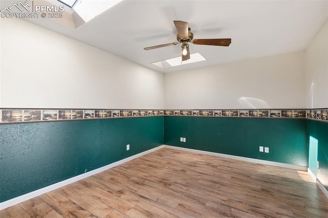 unfurnished room with a ceiling fan, a skylight, baseboards, and wood finished floors