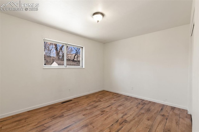 unfurnished room featuring baseboards, visible vents, and hardwood / wood-style floors