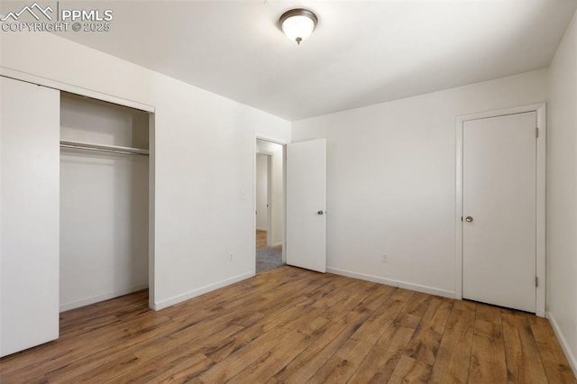 unfurnished bedroom featuring a closet, wood-type flooring, and baseboards