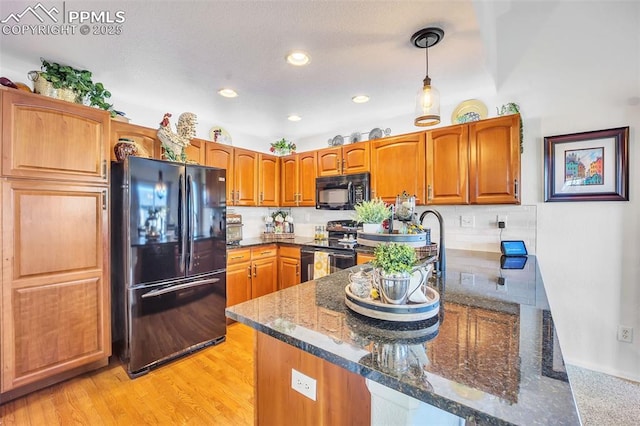 kitchen featuring dark stone countertops, light wood-type flooring, a peninsula, black appliances, and tasteful backsplash