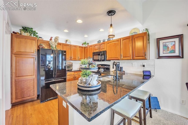 kitchen with black appliances, dark stone countertops, light wood-style floors, a peninsula, and a breakfast bar area