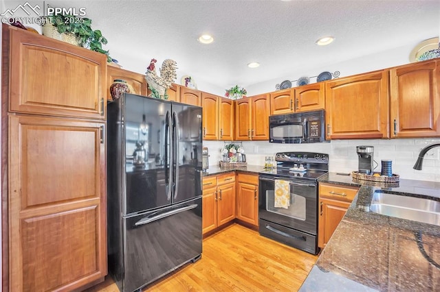 kitchen with dark stone counters, black appliances, light wood-style floors, and a sink