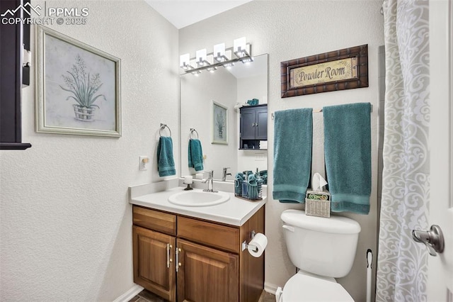 bathroom with toilet, vanity, and a textured wall