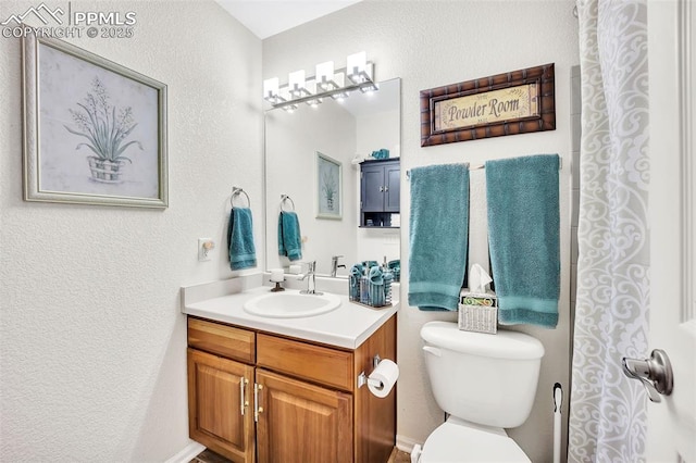 bathroom with vanity, toilet, and a textured wall