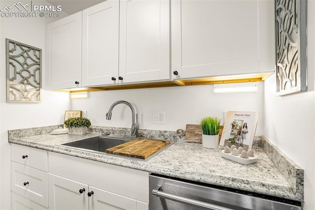 kitchen with light stone counters, stainless steel dishwasher, a sink, and white cabinetry