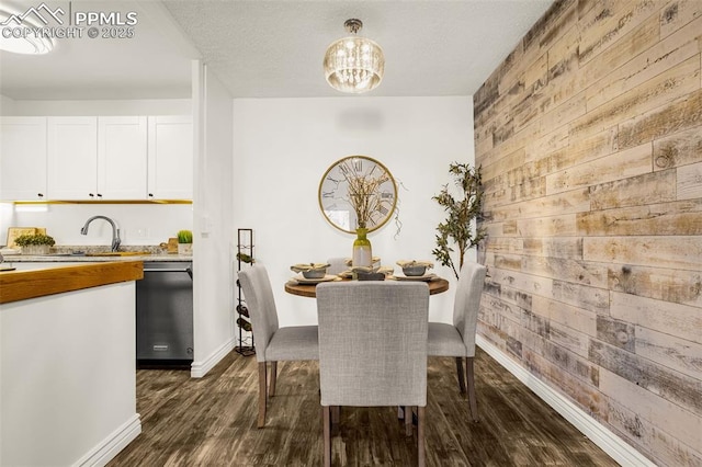 dining area with dark wood finished floors, wooden walls, baseboards, and an inviting chandelier